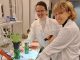 Laura Wey (vas.) ja hänen tutkimusassistenttinsa Venla Orpana laboratoriossa. Pöydällä on biosähkölaitteisto, jonka alaosassa on fotosynteettisiä bakteereja ja päällä rairuohoa.